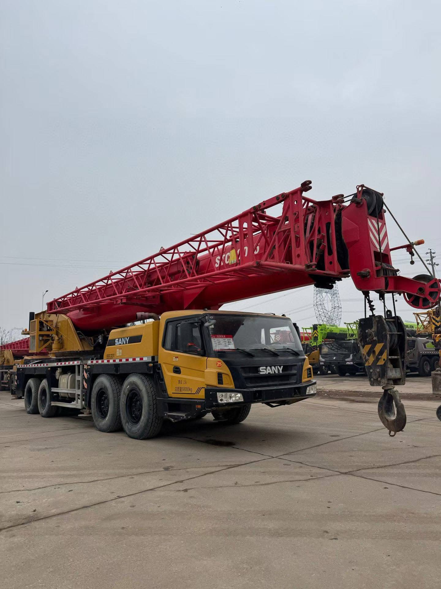 SANY truck crane with yellow and black color scheme, operating on construction site with industrial background, professional heavy machinery photography